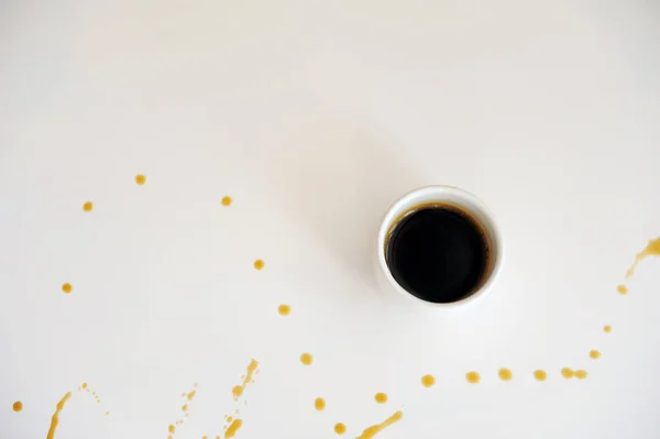 Ένα φλιτζάνι εσπρέσο σε μια λευκή επιφάνεια πιτσιλισμένο με σταγόνες καφέ — Φωτογραφία Αρχείου