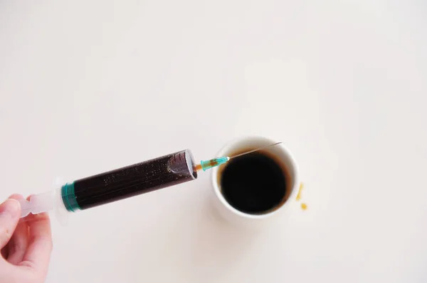 Un expreso mecanografiado en una jeringa médica en la mano sobre una taza. Símbolo de adicción a la cafeína. Fondo blanco aislado — Foto de Stock