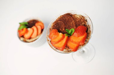 Martini bardağında tiramisu tatlısı. Çilek dilimleri ve nane ile süslenmiş. Üst Manzara. Beyaz arkaplan, izole