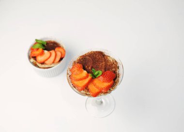 Martini bardağında tiramisu tatlısı. Çilek dilimleri ve nane ile süslenmiş. Üst Manzara. Beyaz arkaplan, izole