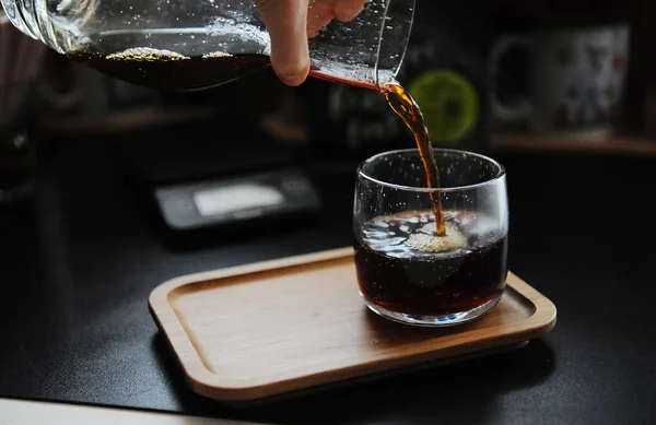 Elaboración manual de bodegones. Verter el café de filtro de la jarra en el vidrio. Bandeja de bambú. Estética de velocidad de la tercera ola — Foto de Stock