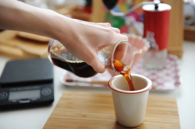 Manual brewing still life. Pouring filter coffee from glass jug into cup. Bamboo board. Third wave specialty aesthetics