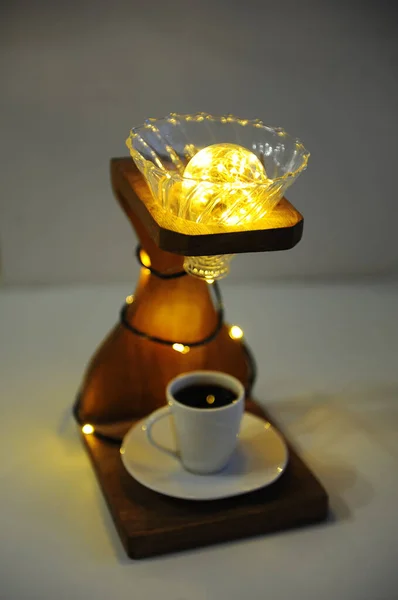 Creative art handmade lamp made of drip coffee stand, v60 dripper and lights. Cup of black coffee in the lower board. Specialty third wave coffee concept