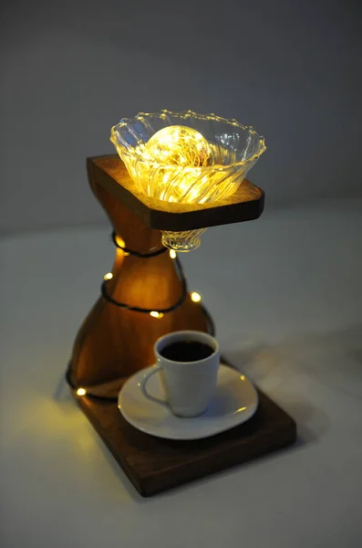 Creative art handmade lamp made of drip coffee stand, v60 dripper and lights. Cup of black coffee in the lower board. Specialty third wave coffee concept