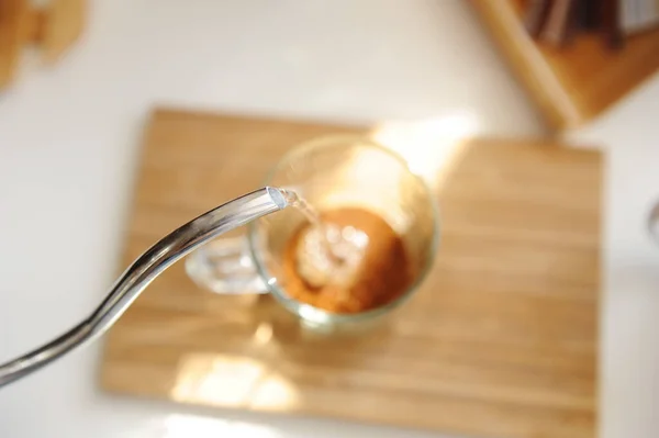 Пивоварение кофе в кружке. Выливание воды из гусиного чайника в стеклянную чашку со свежемолотым кофе вид сверху. Сосредоточьтесь на чайнике — стоковое фото