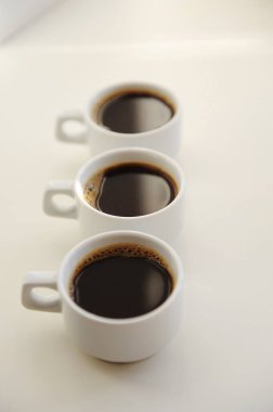 Beyaz arka planda birbiri ardına koyu kahveyle üç beyaz fincan.