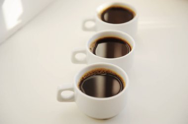 Beyaz arka planda birbiri ardına koyu kahveyle üç beyaz fincan.