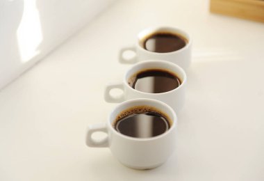 Beyaz arka planda birbiri ardına koyu kahveyle üç beyaz fincan.