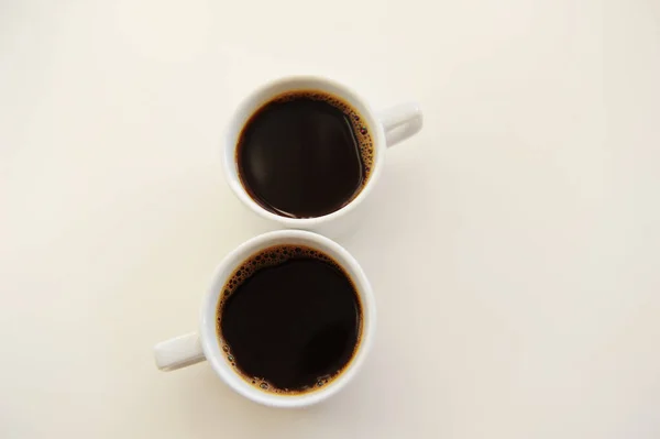 Чёрный кофе в двух белых чашках в форме восьмерки на белом фоне — стоковое фото