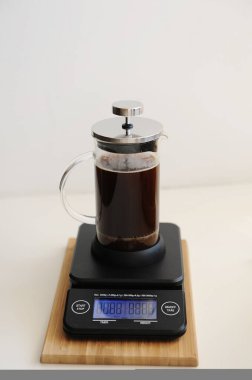 Brewing coffee in french press. Plunger down. On black electronic timer scales. clipart