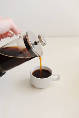 French press 'ten beyaz fincana kahve dökülüyor. Beyaz arkaplan