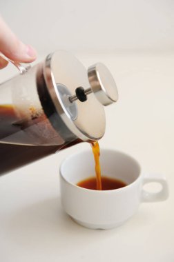 French press 'ten beyaz fincana kahve dökülüyor. Beyaz arka plan. Kapat.