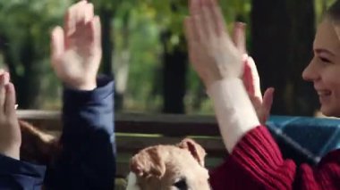 Parkta bankta oturan oynayan iki kız kardeş. Ön planda bir köpektir.