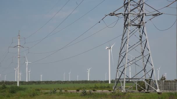Вітрові турбіни на задньому плані з лініями електропередач, що несуть електрику на передньому плані . — стокове відео