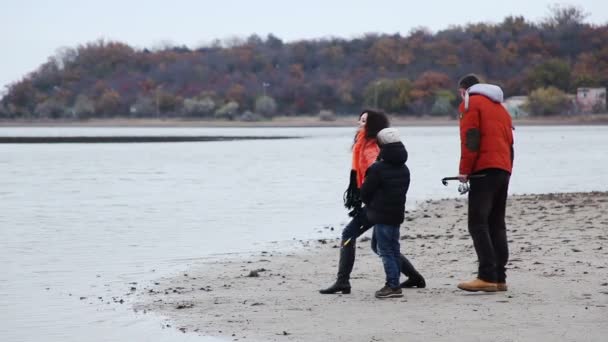 Los padres con su hijo pequeño arrojan piedras al lago . — Vídeos de Stock