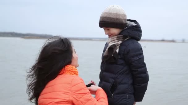 Recreación en la orilla del río. Mamá endereza sombrero y bufanda a su hijo . — Vídeos de Stock