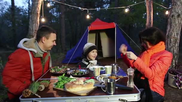 Familia joven y feliz sentada a la mesa y hablando, bosque otoñal . — Vídeos de Stock