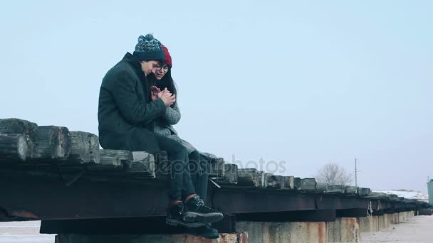 Man en vrouw zitten op de brug en de warme elkaars handen. — Stockvideo