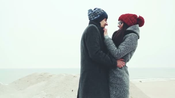 Young couple standing on the winter beach, rubbing his hands together. — Stock Video