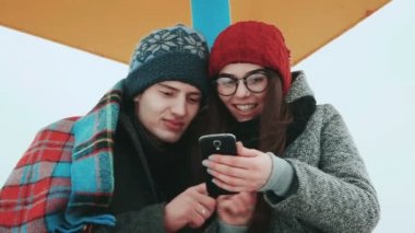 Sahilde bir akıllı telefon, arka planda gri gökyüzü oynarken Çift