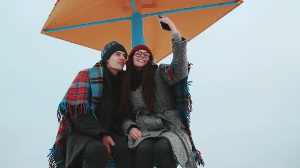 Duas pessoas atraentes, cobertas com um cobertor, fazem selfie contra o céu cinzento . — Vídeo de Stock