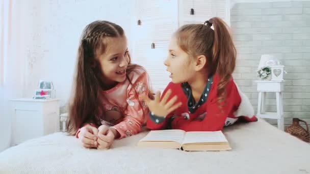 Två små vänner, finns i pyjamas och de läser bok. De prata och diskutera boken. — Stockvideo