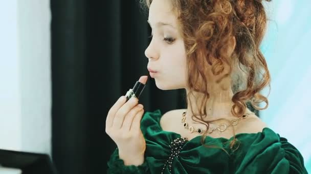 Pequena senhora em um vestido verde sentado na frente de um espelho e batom . — Vídeo de Stock