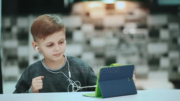 Retrato de criança menino loiro brincando com um computador tablet digital, ouvindo música com fones de ouvido . — Vídeo de Stock