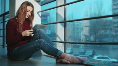 Çekici kız pencere tarafından katta oturan laptop çalışma.