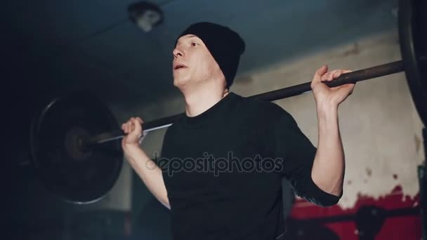 Hombre musculoso haciendo entrenamiento crossfit en un oscuro gimnasio sombreado levantando pesas sosteniendo una barra en el nivel de la cintura en un concepto de salud y fitness, movimiento redondo tiro de cerca . — Vídeo de stock