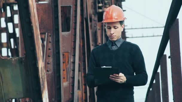 Un joven ingeniero escribe en un portapapeles — Vídeo de stock