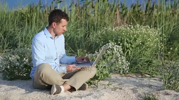 Człowiek siedzi na plaży z laptopem — Wideo stockowe