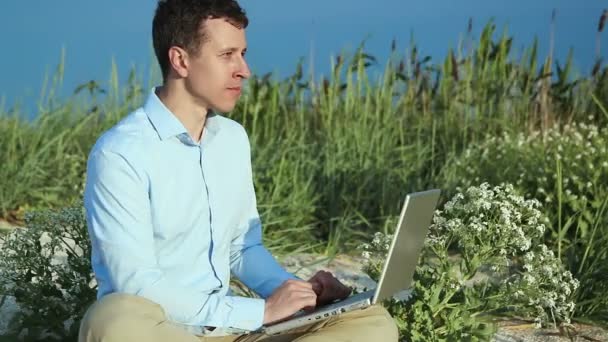 Ο άνθρωπος που κάθεται στην παραλία με ένα laptop. Ελεύθερος επαγγελματίας — Αρχείο Βίντεο