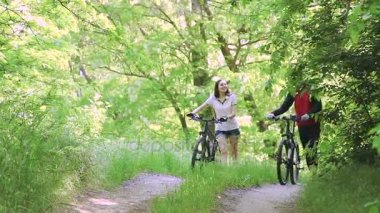 Yaz aylarında parkın içinden Bisikletleri ile yürürken canlı konuşmak güzel genç Çift