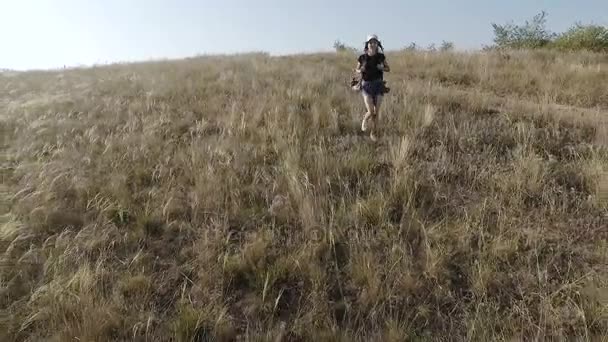 A girl with a backpack on her shoulders runs away from a steep slope. — Stock Video