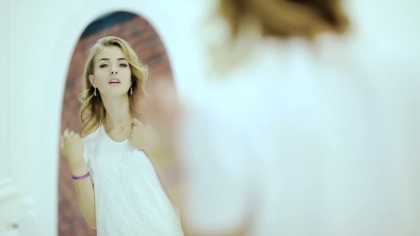 Schöne junge Frau in weißem Hemd, die ihr Spiegelbild im Spiegel betrachtet — Stockvideo