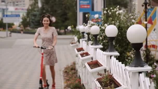 Красива дівчина їде електричним скутером на вуличному тротуарі — стокове відео