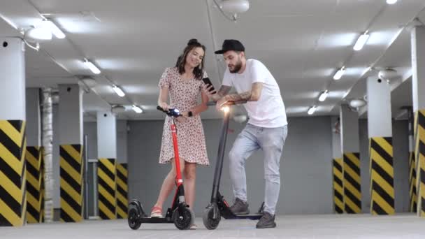 Chico y chica uso de teléfono en scooters eléctricos de bajo ángulo tiro — Vídeo de stock