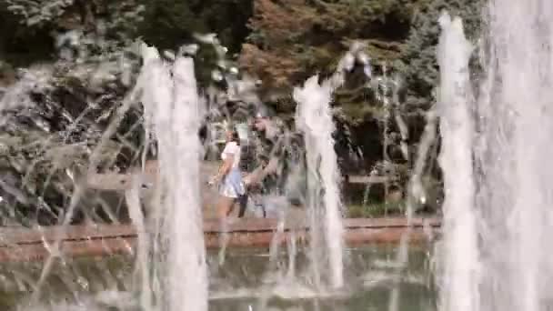 Guy and girl go on electric scooters around fountain in park — Stock Video