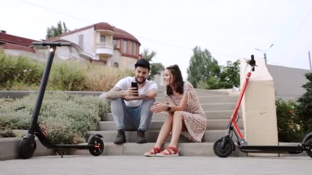 Par vilar från ridning elektriska skotrar och sitter på trappor — Stockvideo