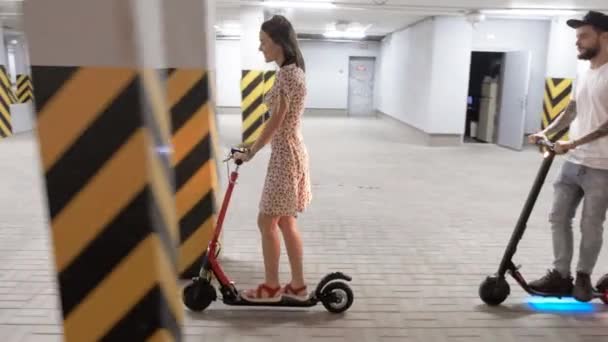 Dziewczyna i facet jeżdżą na skuterach elektrycznych na podziemnym parkingu.. — Wideo stockowe