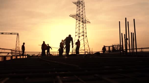 Silhouetten van werknemers op een bouwplaats bij zonsondergang. — Stockvideo