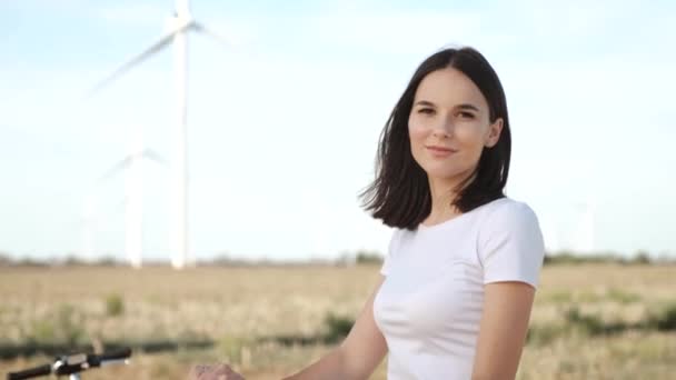 Attraktives Mädchen mit einem Elektroroller vor dem Hintergrund von Windkraftanlagen. — Stockvideo