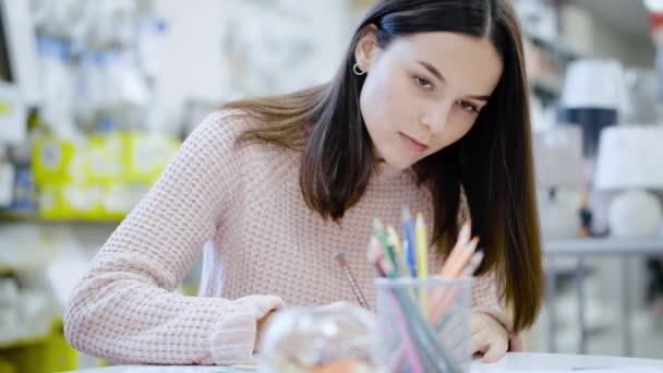 Девушка садится за стол и рисует карандашами — стоковое видео