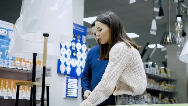 Casal jovem escolher uma lâmpada de noite em um supermercado — Vídeo de Stock