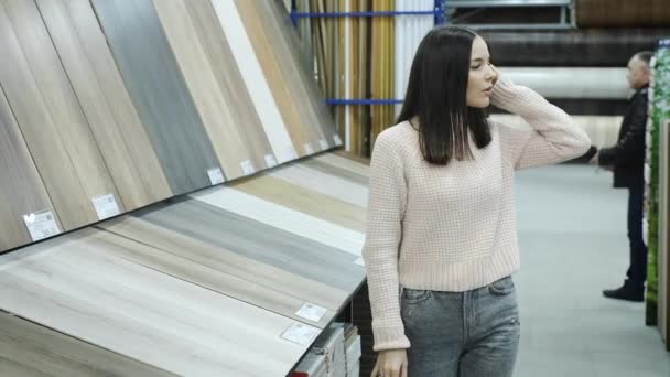 Uma menina em um supermercado de materiais de construção escolhe um laminado — Vídeo de Stock