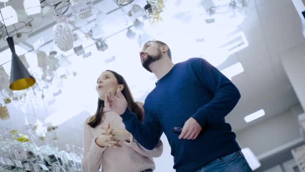 Een getrouwd stel in een supermarkt kiest een kroonluchter voor hun appartement. — Stockvideo