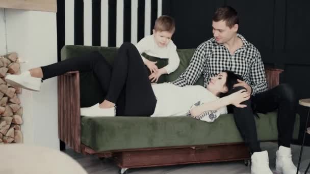 Hamile bir kadın, kocasının kucağında, dört yaşındaki oğullarıyla birlikte sade bir ortamda yatıyor.. — Stok video