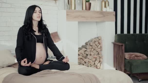 Беременная брюнетка с длинными вьющимися волосами сидит в специальной позе — стоковое видео