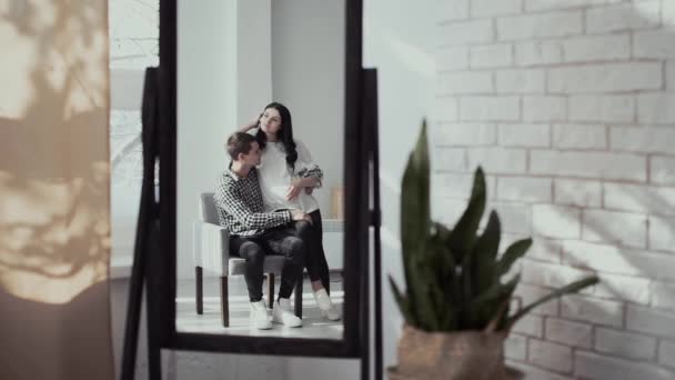 Hosszú hajú feleség és jóképű férfi ölelés ül barna szék — Stock videók